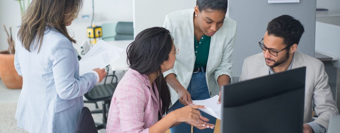 Group of young people gather around a laptop in an office to discuss inclusivity and diversity in small business.