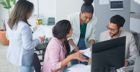 Group of young people gather around a laptop in an office to discuss inclusivity and diversity in small business.