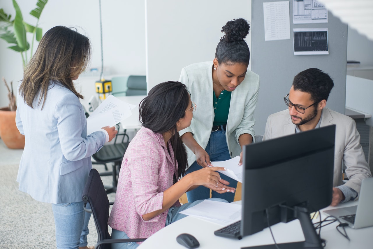 Group of young people gather around a laptop in an office to discuss inclusivity and diversity in small business.